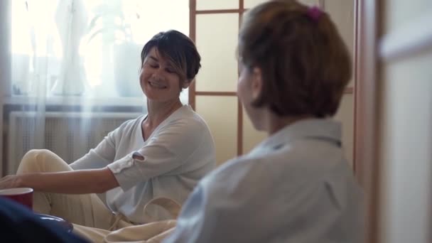 Duas mulheres adultas a passarem tempo juntas em casa. Duas elegantes namoradas maduras relaxando em casa, conversando e compartilhando notícias. Conceito de amizade, bem-estar, vida feliz. Movimento lento . — Vídeo de Stock