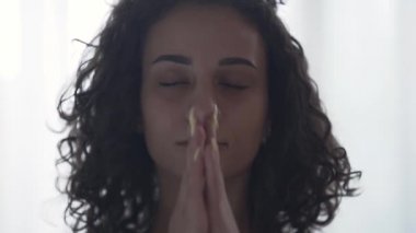 Gözlerini kapatan ve derin nefes alan kıvırcık rahatlatıcı genç bir kadının yakın çekim portresi. Evde ya da stüdyoda yoga yapan kız. Ruhsal gelişim