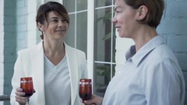 Balkonda duran şarap içme rahatlatıcı iki zarif olgun kız. İki yetişkin kadın evde birlikte vakit geçiriyor. Dostluk, sağlıklı yaşam, mutlu yaşam kavramı.