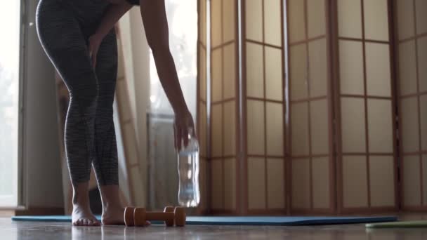 Aantrekkelijke jonge vrouw zittend op de yoga mat vouwen handen in Namaste gebaar. Yoga lessen of meditatie thuis of in de Studio. De fles met het water staat op de vloer. Gezonde levensstijl — Stockvideo