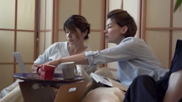 Две взрослые женщины, вместе пьющие чай или кофе, смотрят кино на ноутбуке. Две элегантные зрелые девушки расслабляются дома. Концепция дружбы, здоровья, счастливой жизни — стоковое видео