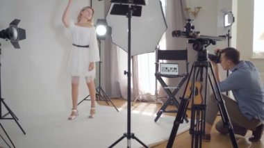 Fotoğraf çekiminin sahne arkası. Profesyonel fotoğrafçı stüdyoda beyaz arka plan üzerinde poz sevimli kadın fotoğrafları çekiyor. Moda dergisi stüdyo photoshoot.