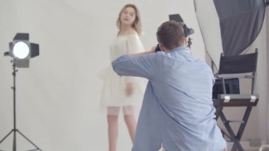 Fotoğraf çekiminin sahne arkası. Fotoğrafçı stüdyoda beyaz arka plan üzerinde duran çekici kadının fotoğraflarını çekiyor. Moda dergisi stüdyo photoshoot.
