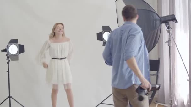 Nos bastidores da sessão fotográfica. Fotógrafo profissional dançando com um modelo antes de tirar fotos no estúdio em fundo branco. Fotografia, profissão, sessão de fotos . — Vídeo de Stock