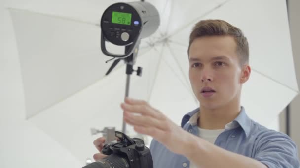 Retrato de un joven fotógrafo masculino tomando fotos con su cámara sobre fondo blanco en el estudio. Fotografía, profesión, sesión de fotos . — Vídeos de Stock