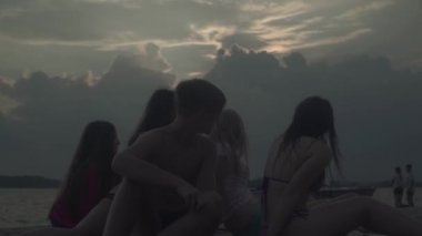 Gençler nehir kıyısında dinleniyor. Gençler nehir boyunca koşup eğleniyorlar. Genç adam gitarla koşuyor. Su her yöne sıçrar..