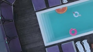 Havuzun tepesinden parlak renkli şişirilebilir dairelerin görüntüsü. Havuzun üst manzarası, renkli şişirilebilir daireler ve havuzun kenarında duran güneş sandalyeleri..
