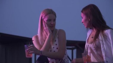 Bir gece kulübünde kokteyl içen gülümseyen iki kız. Kokteyllerle oturan iki kız arkadaş bir yaz kulübünde sohbet ediyorlar..