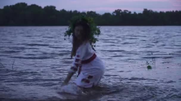 穿着白衣头戴花环的小女孩 女孩走进河里 用手触摸着水 美丽的女孩在泼水 — 图库视频影像