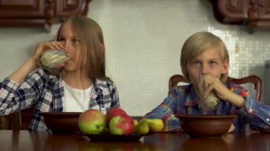 Tatlı çocuk ve kız bardaktan süt içiyor. Kardeşler mutfaktaki masada oturarak sağlıklı içeceklerinin tadını çıkarırlar. Sağlıklı yaşam tarzı