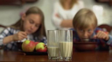 Arka planda mısır gevreği yiyen mutlu küçük kardeşler ön plandaki masada iki bardak sütlü süt içerken. Mutlu dost canlısı kardeşler, afiyet olsun.