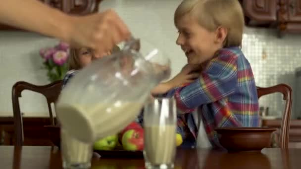 母亲的手把牛奶倒在玻璃杯里给前景看好的孩子们喝 两个孩子在后方互相争斗 互相推挤 健康的生活方式 — 图库视频影像
