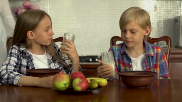 ガラスから牛乳を飲む愛らしい子供たち 兄弟はキッチンのテーブルに座って健康的な飲み物を楽しんでいます 健康的なライフスタイル — ストック動画