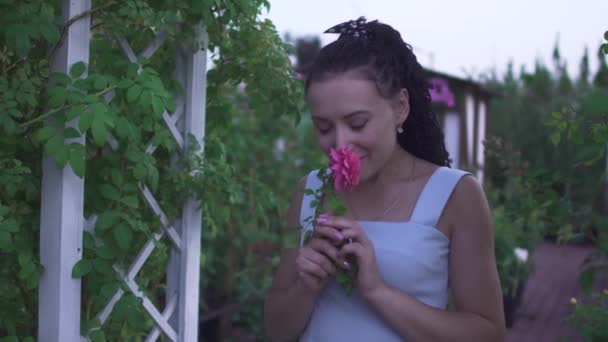 身穿白衣的漂亮的黑发女士在花园里闻到了花朵的芬芳 女人看着天空 在绿色花园等待户外时间 女人又笑又开心 — 图库视频影像
