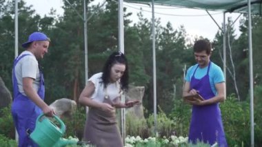 Bahçe çalışanları iş başında. Bahçe merkezinde iki erkek ve bir kız çalışıyor. Çiçekleri sulama kabıyla sulayan bir adam. Adam ve kız tablet ve telefondaki bilgileri kaydediyor..