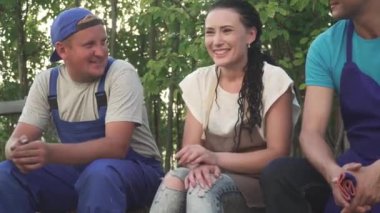 Üniformalı bahçıvanlar saman çantasında oturuyorlar. Üç erkek ve bir kadın birlikte konuşuyor. İşçiler işten sonra dinlenir