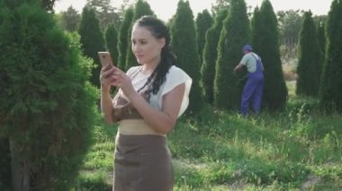 Bahçıvanlar ağaçlarla ilgilenir. Kadın dalların fotoğrafını çeker ve erkek şekil vermek için yaprakları keser. İnsanlar işlerini dikkatli yaparlar. Kamera sola hareket ediyor.