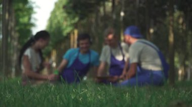 Bahçıvan ekibi işten sonra sahada dinleniyor. İnsanlar bulanık ve bulanık. Erkekler ve kadınlar dostça konuşurlar.