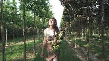 Kahverengi üniformalı kadın bahçede yürüyor. Hanımefendinin elinde birkaç dal var. Kadın mutlu ve gülümsüyor. İşinden zevk alan birinin portresi