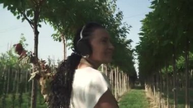 Kahverengi üniformalı kadın bahçede yürüyor. Hanımefendinin elinde birkaç dal var. Kadın mutlu ve gülümsüyor. İşinden zevk alan birinin portresi