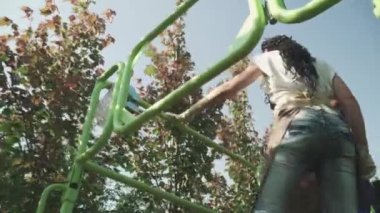 Mavi üniformalı bahçıvan dalı kesip asansörde duran yardımcısına verdi. İnsanlar makine asansörünü kullanarak ağaçları önemser. Ağaçlar bahçede düzenli sırada yetişir. Aşağıdan ateş ediliyor.