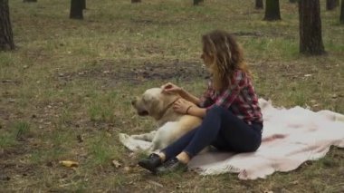 Genç kadın ormanda köpekle vakit geçiriyor, battaniyeye uzanıyor, video çekiyor. 