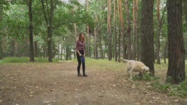 Genç bir kadın köpekle ormanda yürüyor. 