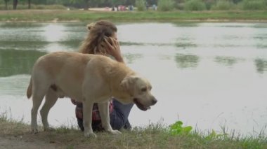 Kıvırcık kadın ve Labrador köpeği nehir suyunun yanında dinleniyor. 