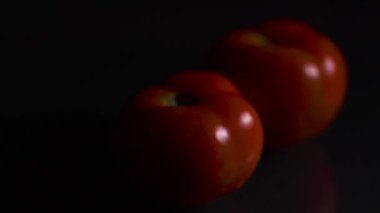 Siyah arka planda domatesler. Domates bir grup domatesin içinde yuvarlanır. Yakın plan. Siyah arkaplan.