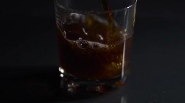 Buz küpleri siyah zemin üzerinde kola olan bir bardağa düşer, video yavaş çekimde.