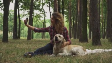 Güzel bayan ormanda köpeğiyle akıllı telefondan selfie çekiyor.