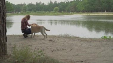Kadın nehir kenarında Labrador köpeği besliyor. 