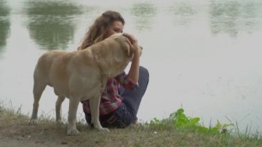 Kıvırcık kadın ve Labrador köpeğinin göl kenarında oturduğu video. 