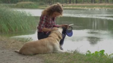 Kıvırcık kadın ve Labrador köpeği göl kenarında dinleniyorlar. 