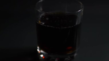 Buz küpleri siyah zemin üzerinde kola olan bir bardağa düşer, video yavaş çekimde.