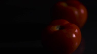 Siyah arka planda domatesler. Domates bir grup domatesin içinde yuvarlanır. Yakın plan. Siyah arkaplan.
