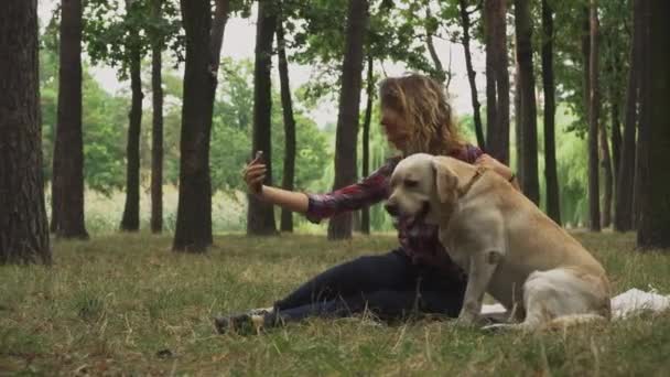 若い女性は森の中でラブラドール犬と携帯電話でセルフィーを作っています ビデオ — ストック動画