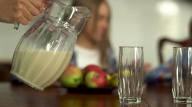 Ön plandaki çocuklar için bardaklara süt döken annenin eli. Arka planda kavga eden ve birbirini iten iki çocuk. Sağlıklı yaşam tarzı