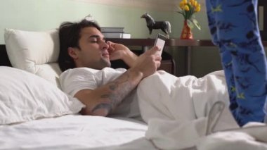 Pijamalı küçük kardeş, sabahları yatakta yatan ağabeyinin yanında zıplayıp dans ediyor..