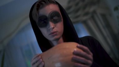 Adamın yüzü transta, yakın plan. Genç adam ruhtan korkuyordu. Elinde balkabağı tutan siyah elbiseli bir adam. Cadılar Bayramı tatili, video 