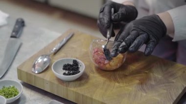 Siyah eldivenli, beyaz restoran üniformalı bir şef ton balığı ve selmonla tabağı süsleyip siyah havyarın içine koyuyor.