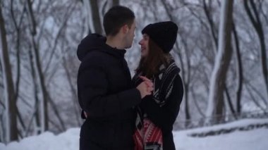 Güzel genç kadın ve erkek kış parkında kar altında gözlerinin içine bakarak konuşur. Adam kadının ellerini ısıtıyor, video. 
