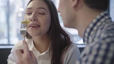 Modern kafede birlikte vakit geçiren genç bir çiftin portresi. Modern kafede oturan tanınmayan bir adam kız arkadaşını besliyor. Güzel bir kadın gülümsüyor ve peçeteyle ağzını siliyor.