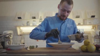 Restoran şefi dairesel metal formunda kesilmiş ton balığı koyuyor ve büyük tabakta yuvarlak bir şekil veriyor. Güzel tabak süslemesi. Aşçı modern mutfakta duruyor, etrafında bir sürü mutfak malzemesi var..