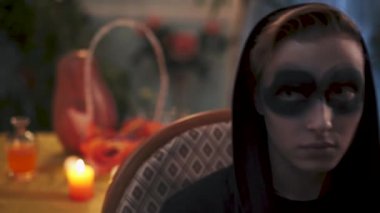 Koyu renk elbiseli genç bir adam sandalyede oturuyor. Sprey kutusuyla siyah daireler çiziyor. Cadılar Bayramı tatili, video 