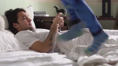 Pijamalı küçük kardeş, sabahları yatakta yatan ağabeyinin yanında zıplayıp dans ediyor..