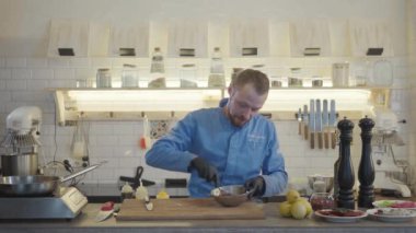 Restoran üniformalı aşçı ve siyah eldivenler modern mutfakta duruyor. Mutfakta bir sürü mutfak gereçleri var ve küçük bir ton balığı parçasıyla karıştırıyorlar..