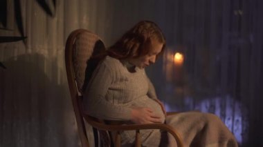 Uzun saçlı hamile bir kadın ilk kez karnında bebeğinin hareketini hissetti. Hanımefendi mutlu ve heyecanlı. Doğmamış çocuk anneyi içeriden tekmeliyor. Kadın sallanan sandalyede ve videoda tek başına vakit geçiriyor. 