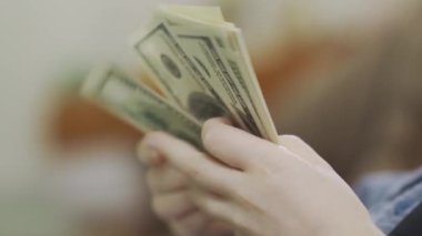 Çocuğun eli bir tomar doları yakın mesafeden tutuyor. Çocuk yavaş yavaş para sayıyor. Arka plan bulanık. Sağlık konsepti, zengin hayat.