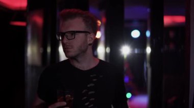 Diskoda elinde bir bardak alkolle dikilen rahat bir adamın portresi. Gözlüklü yetişkin adam kameraya bakıyor ve kokteylini içiyor. Partiye katılanların boş vakitleri